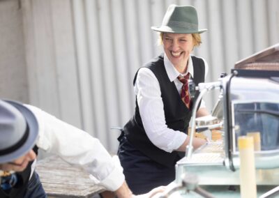Zwei schick gekleidete Baristi haben Freude beim Kaffee Catering an einer Siebträger Espressomaschine Faema e61
